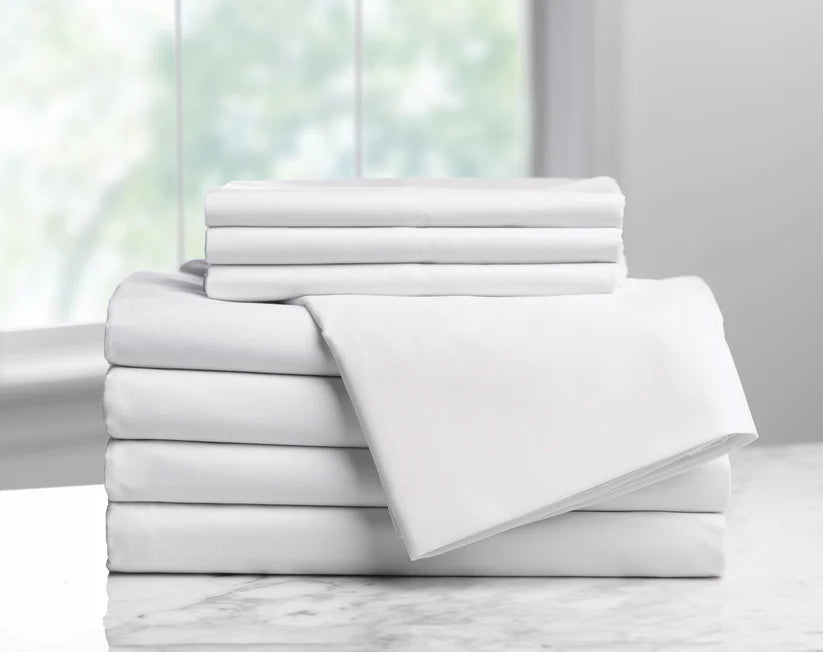 Stack of white bed sheets on a marble surface with a blurred window background